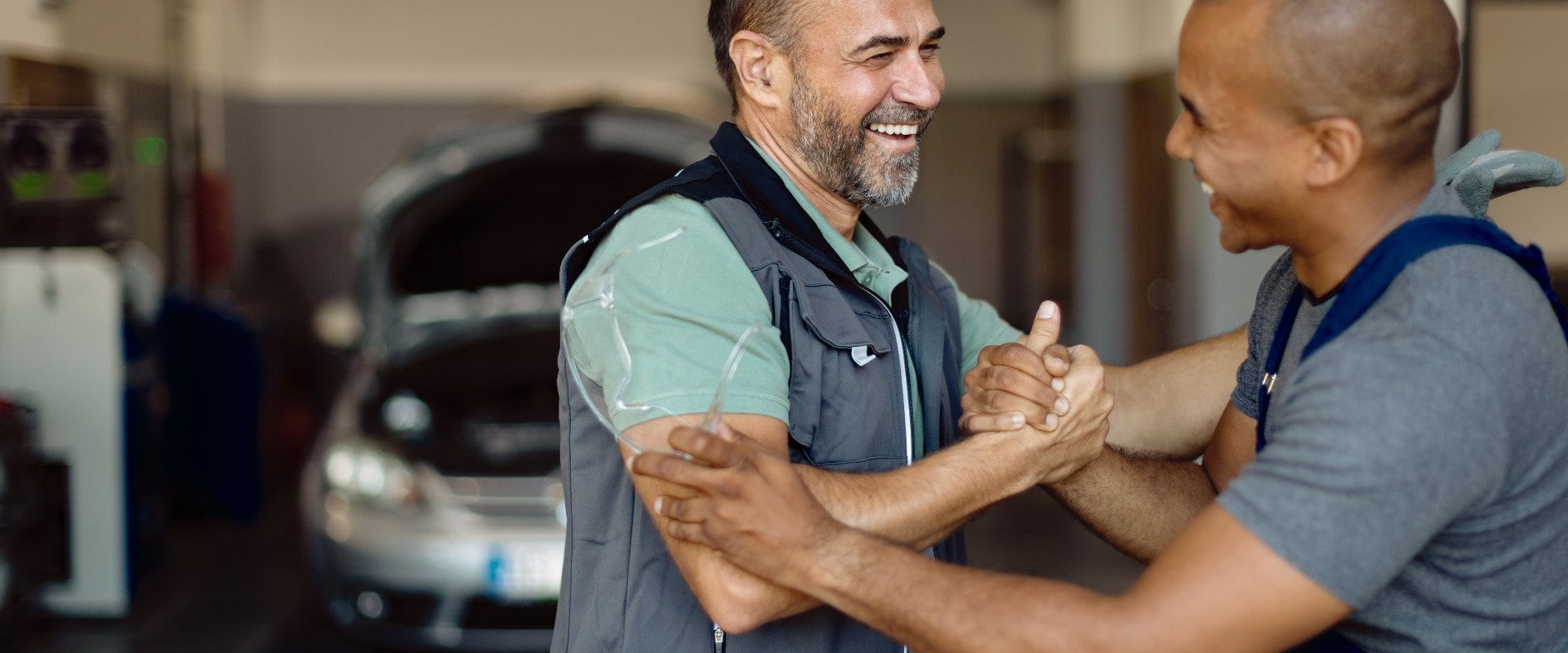 Happy auto mechanics giving each other manly greet at repair shop.